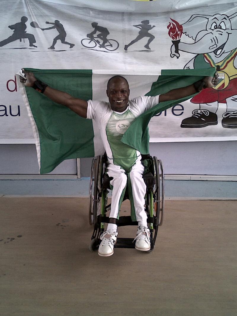 Man in a wheelchair, holding a Nigerian flag and celebrating