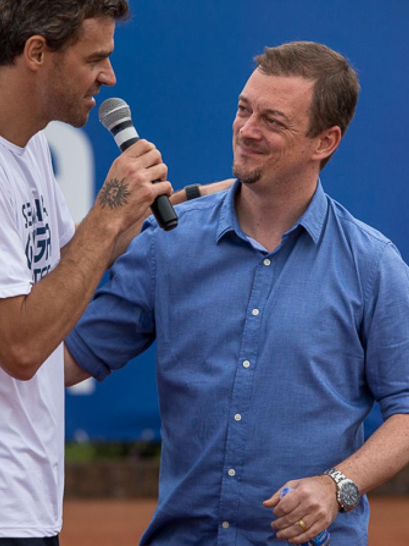 Two men on a stage, on speaking into a microphone