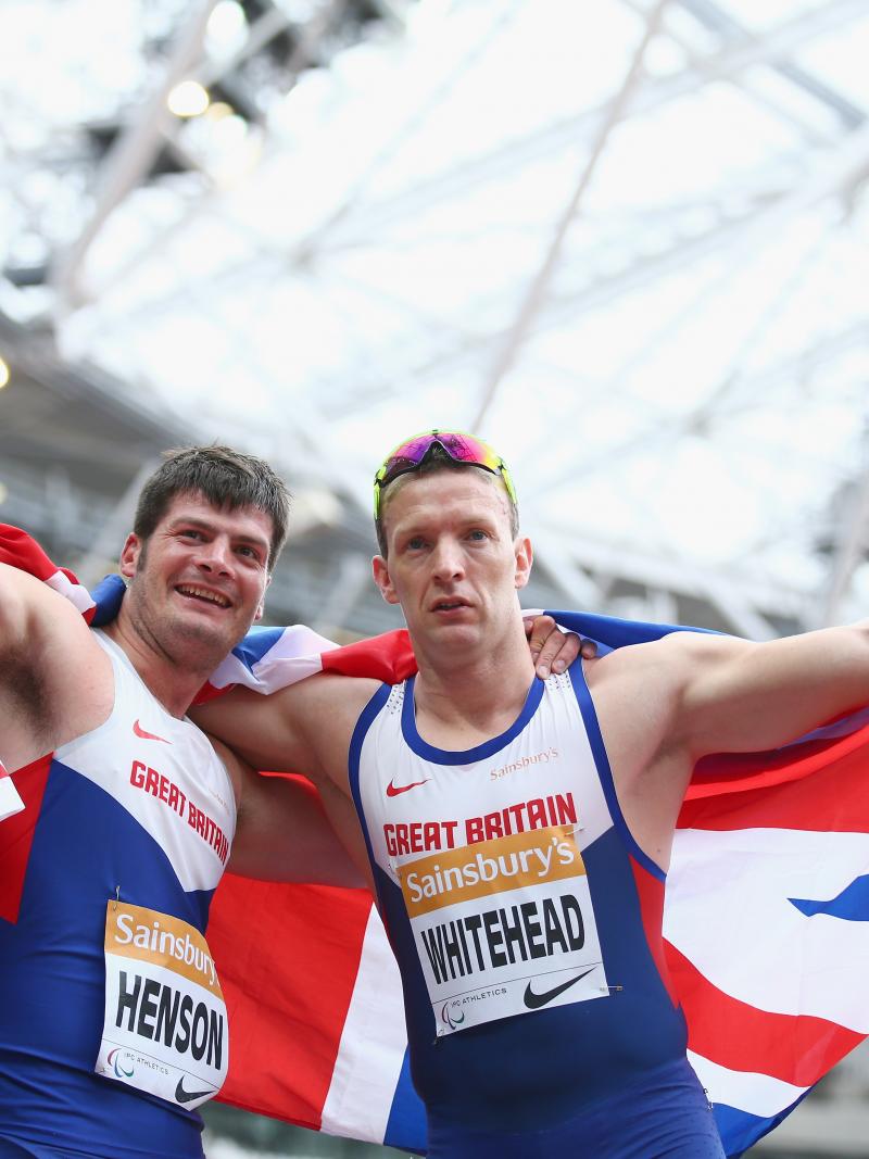 Two men in British racing vests hold a union jack behind them as they celebrate victory,