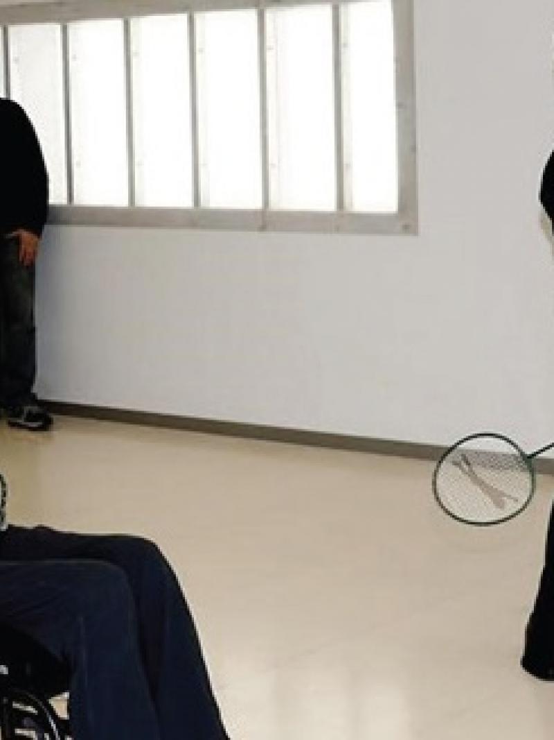 Two men, one standing, one in a wheelchair playing badminton