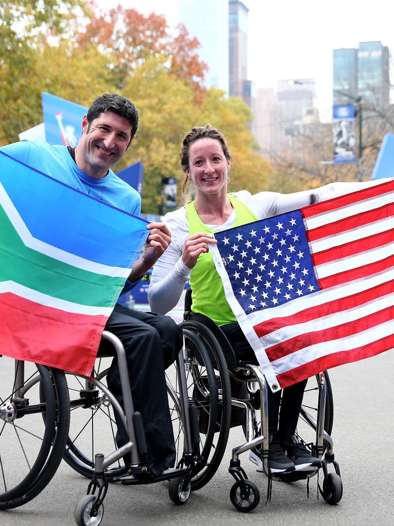 Man and woman in wheelchair hold their countries' respective flags.