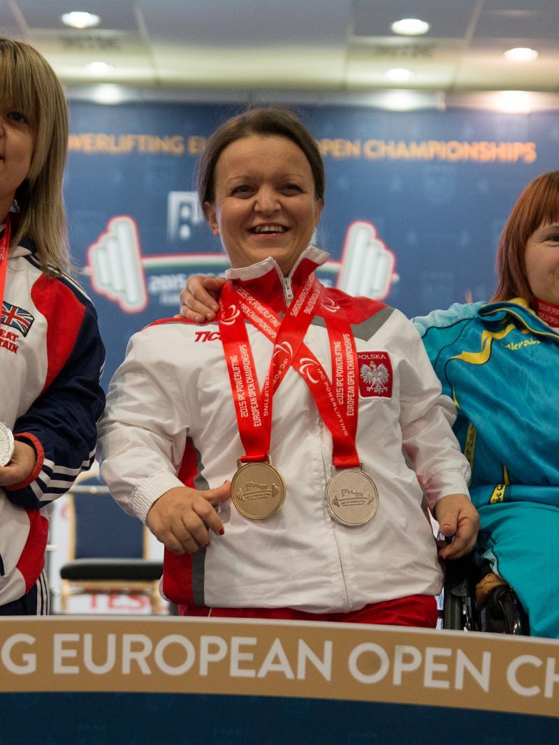 Three women with medals around their necks posing on the podium