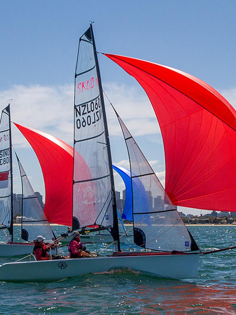 Two boats with red sails on the water in front of a skyline
