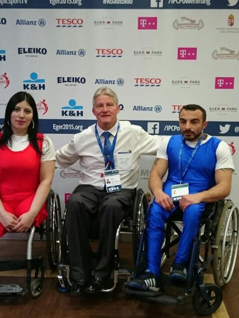 Two athletes posing with a man in front of a branded backdrop