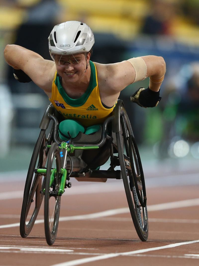 a female from Australia competing in a wheelchair with green and yellow clothes and a white helmet