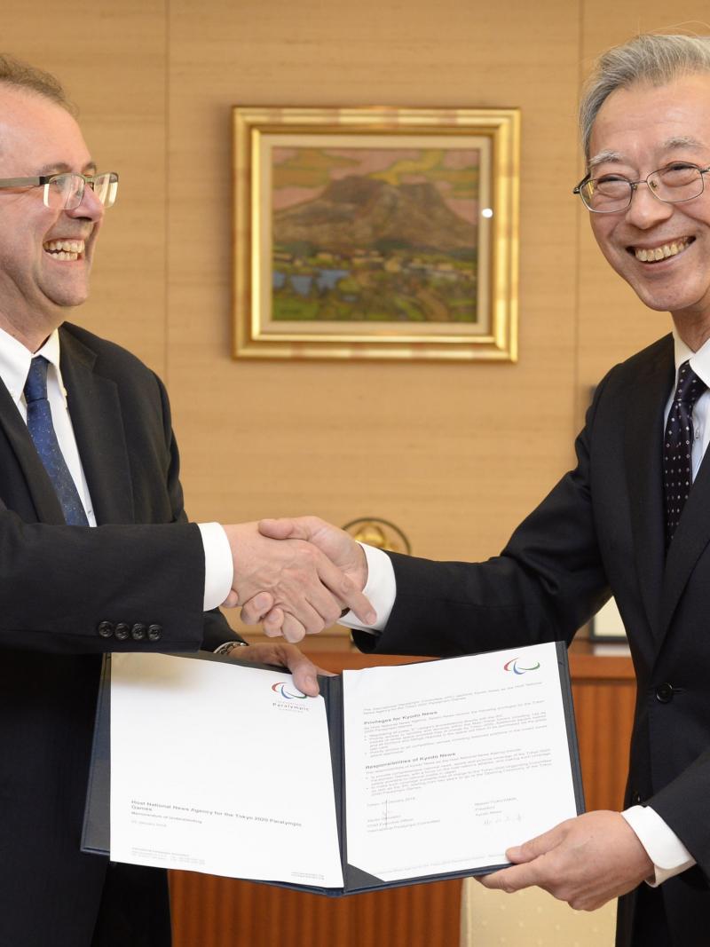 Two men shaking hands, holding a document