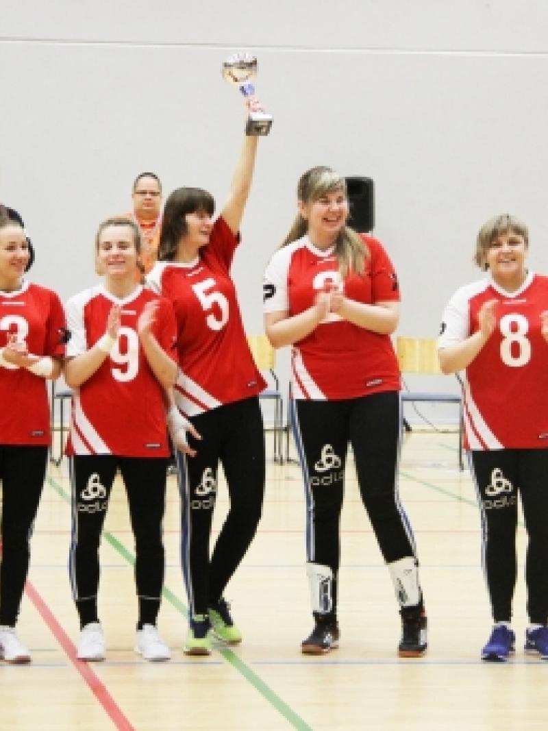 Group of women in red jerseys, showing a trophy, smiling