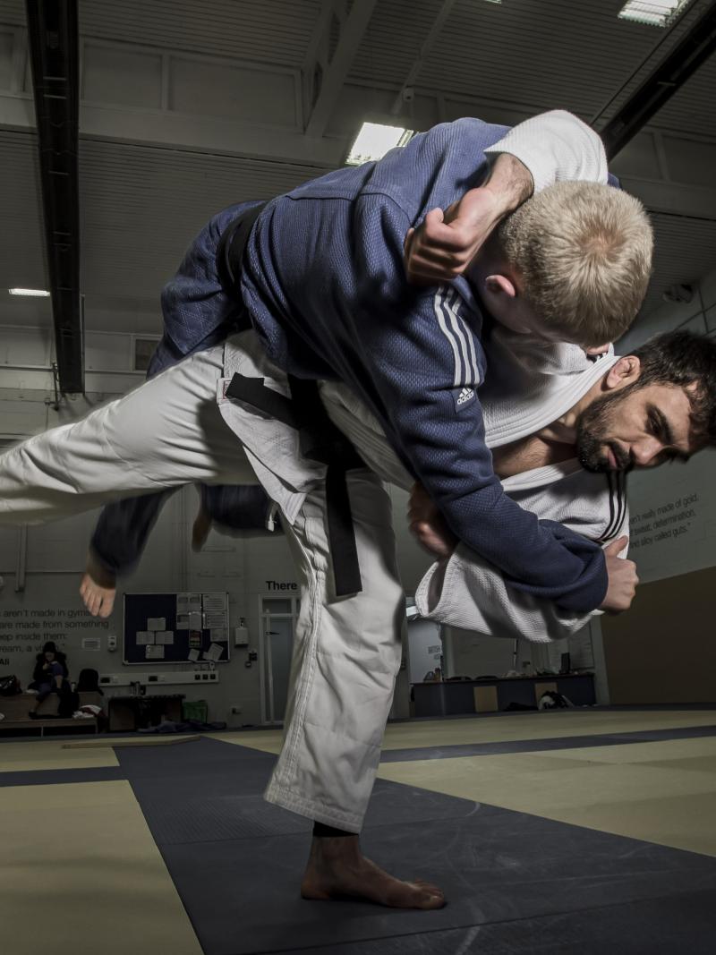 A male judoka in a while suit puts a move on another male judoka in a blue suit. 