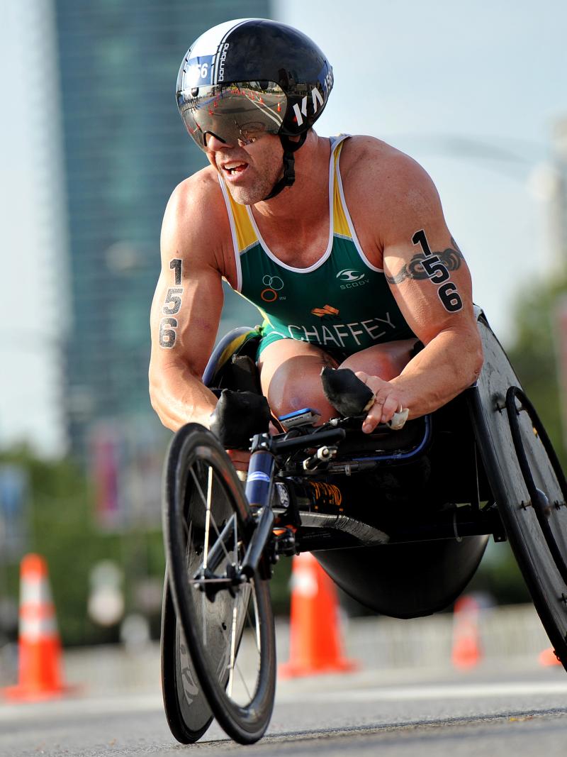 Man in green jersey in a racing wheelchair on a street