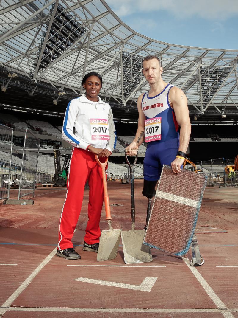 A man and a woman in a stadium, with spadens, working on an athletics track