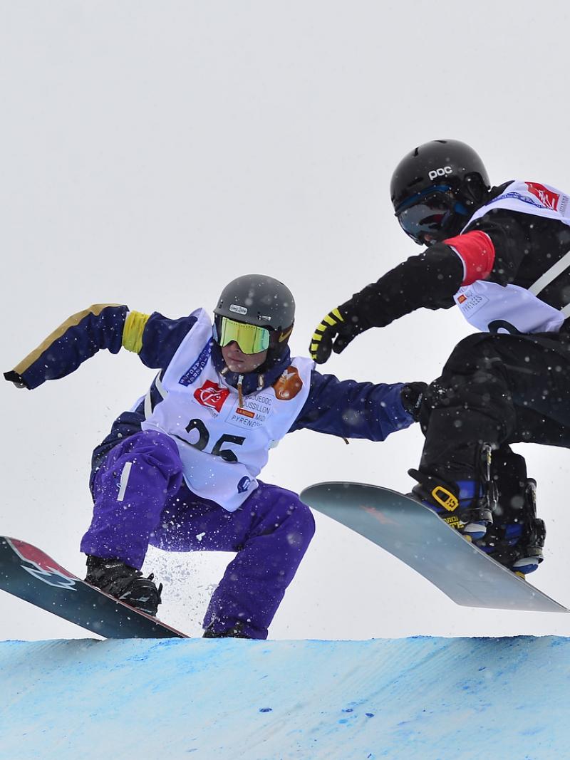 Two snowboarders jumping during a run