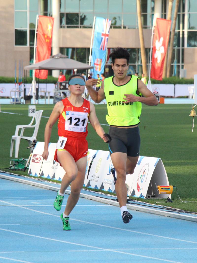A visually impaired runner runs with her guide