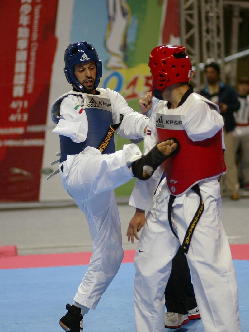 A para-taekwondo athlete does a jump kick to his opponent.
