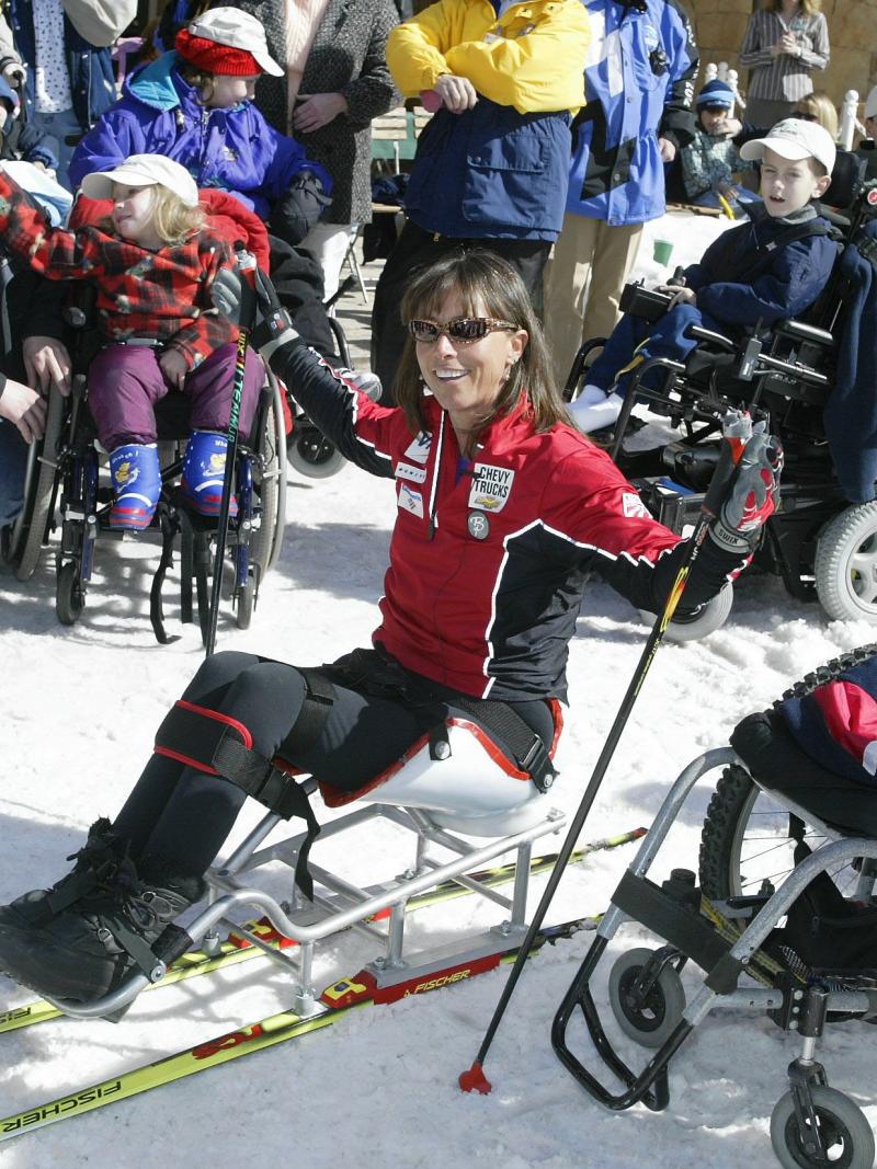 Woman in sit-ski speaks to children.
