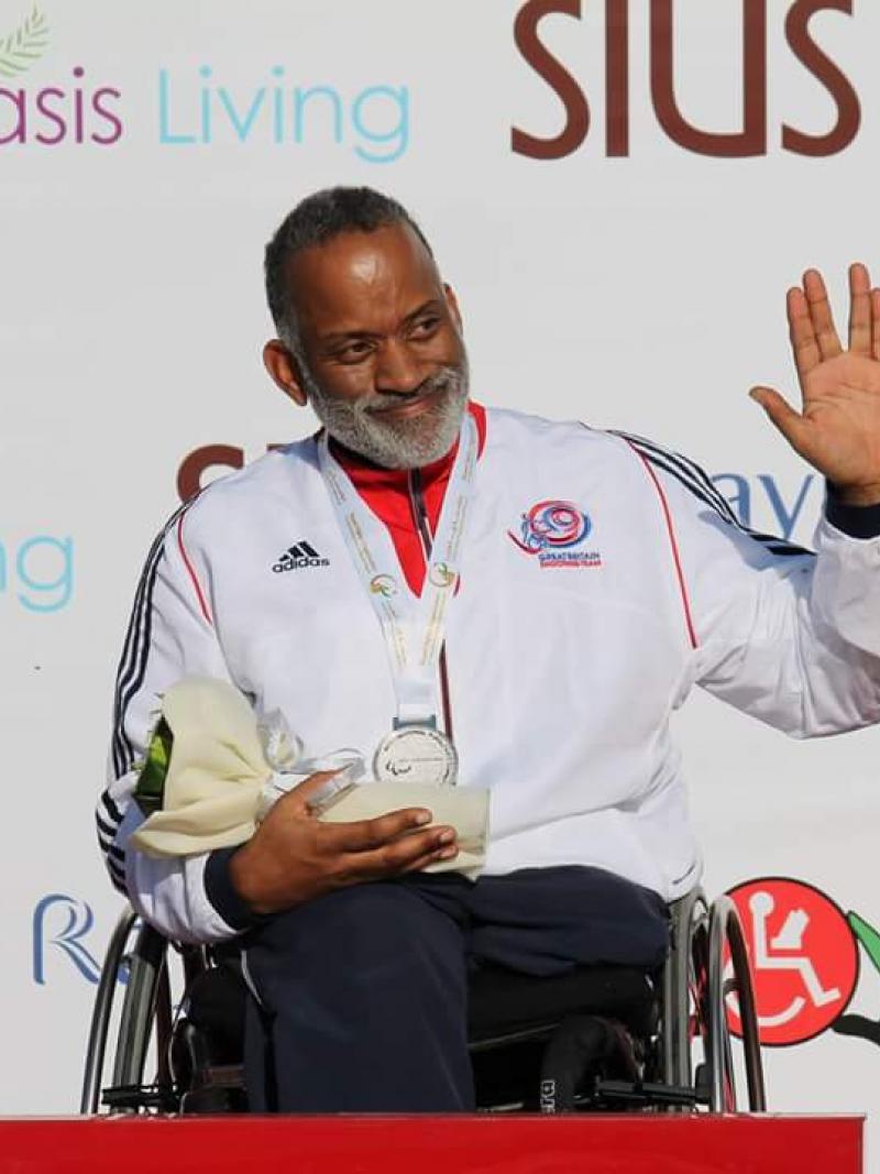 Man in wheelchair holding a medal, waving
