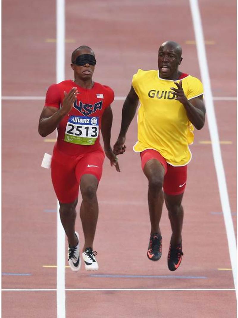 two men running, one with red clothes, one with a yellow t shirt saying guide