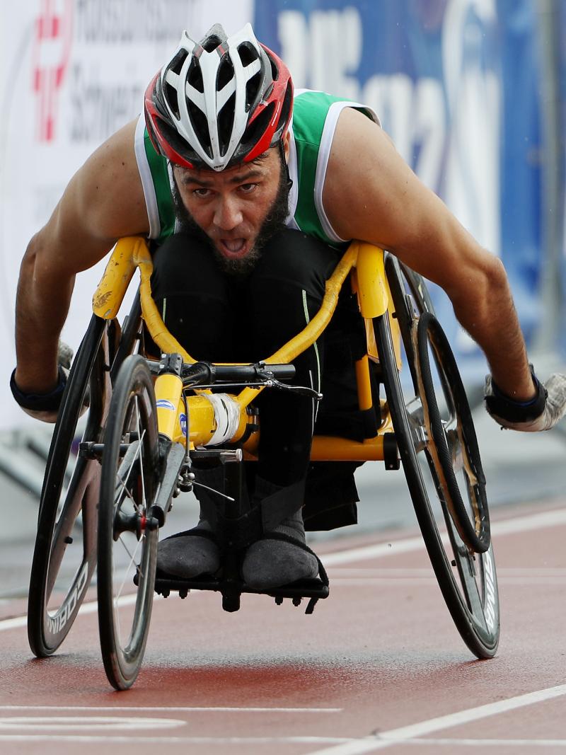 A man in a yellow racing chair pushes forward in the outside lane of a race.