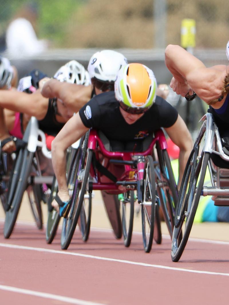 A wheelchair racer leads a line of competitors on a red track.