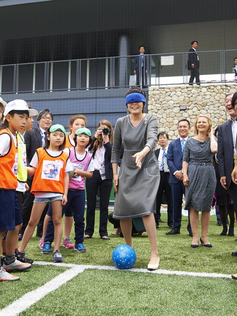 Woman in smart grey dress, blindfolded, surrounded by kids