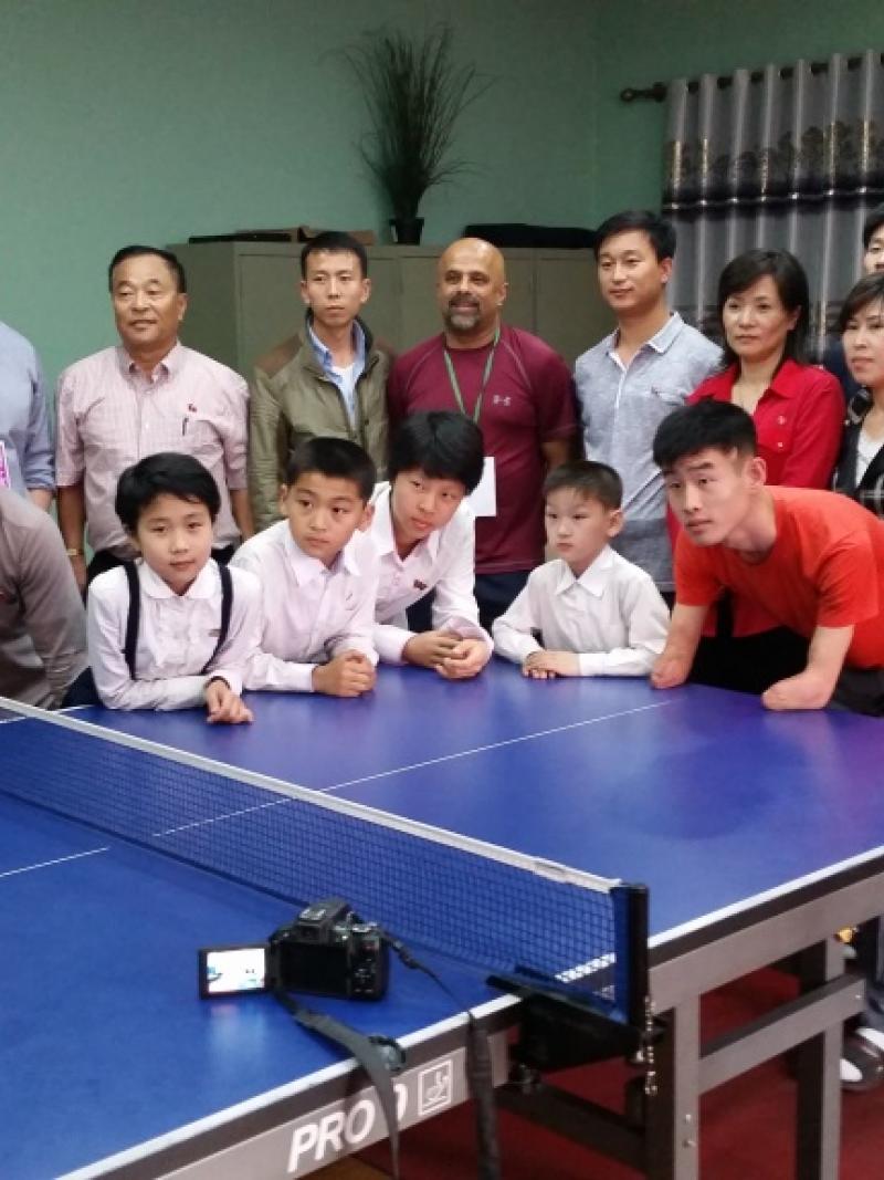 Group picture of kids and adults around a table tennis table