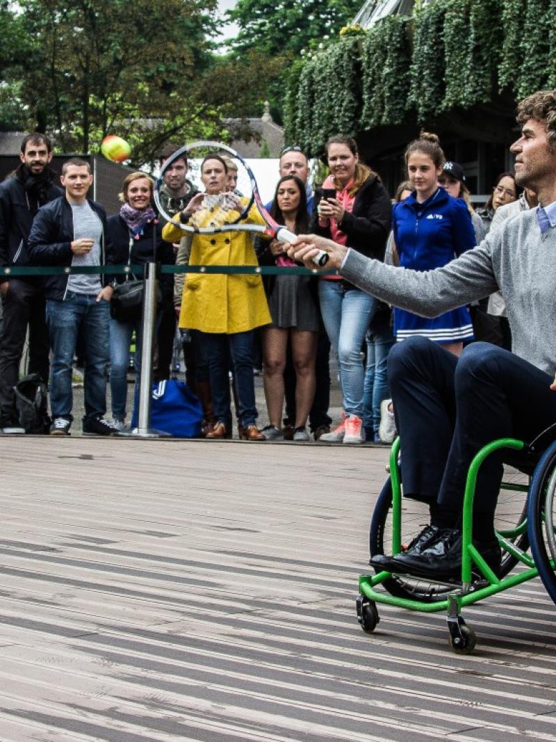 An athlete in a wheelchair hitting a ball with a tennis racket. 