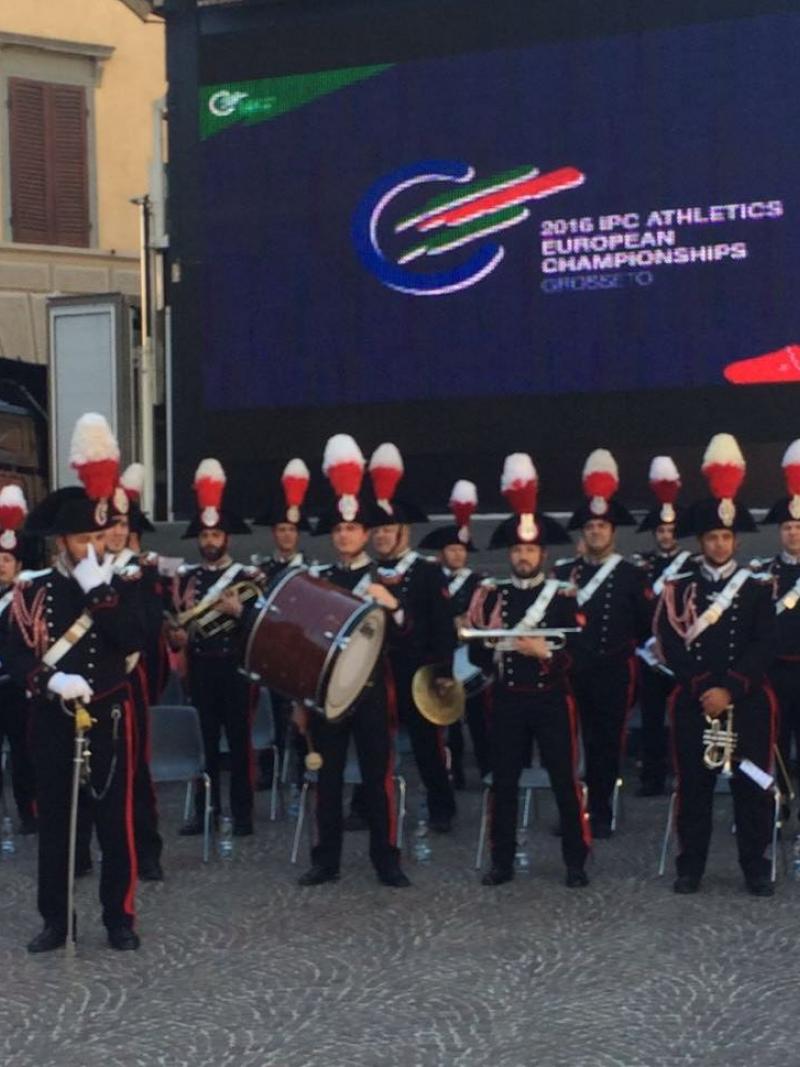 Music band of uniformed men in front of a TV board