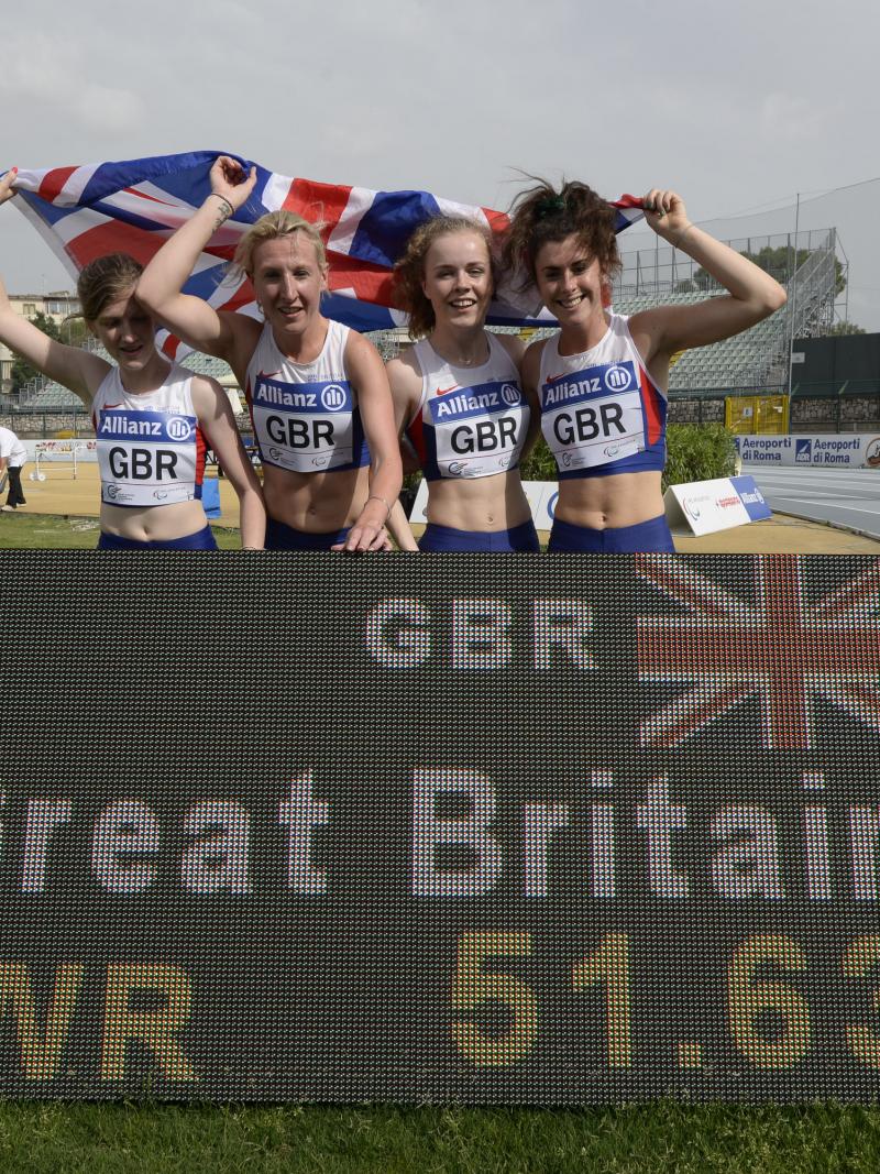 Four girls with British flag post behind a scoreboard