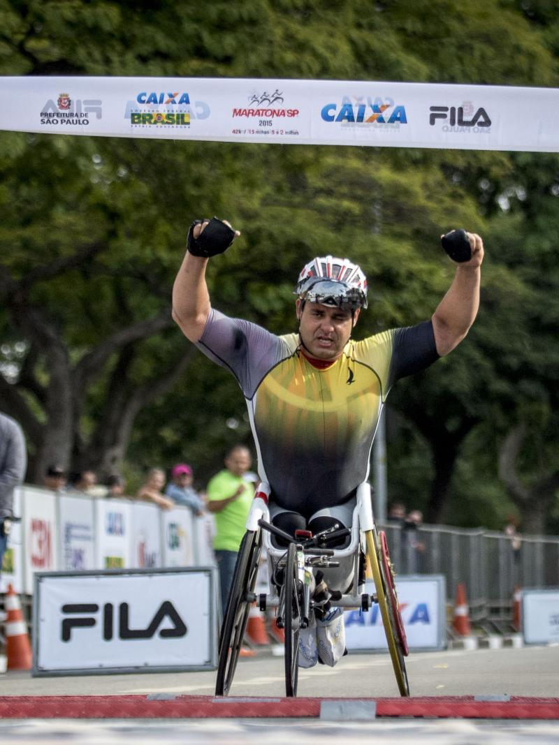 Man in wheelchair raises both arms as he crosses a finishline.