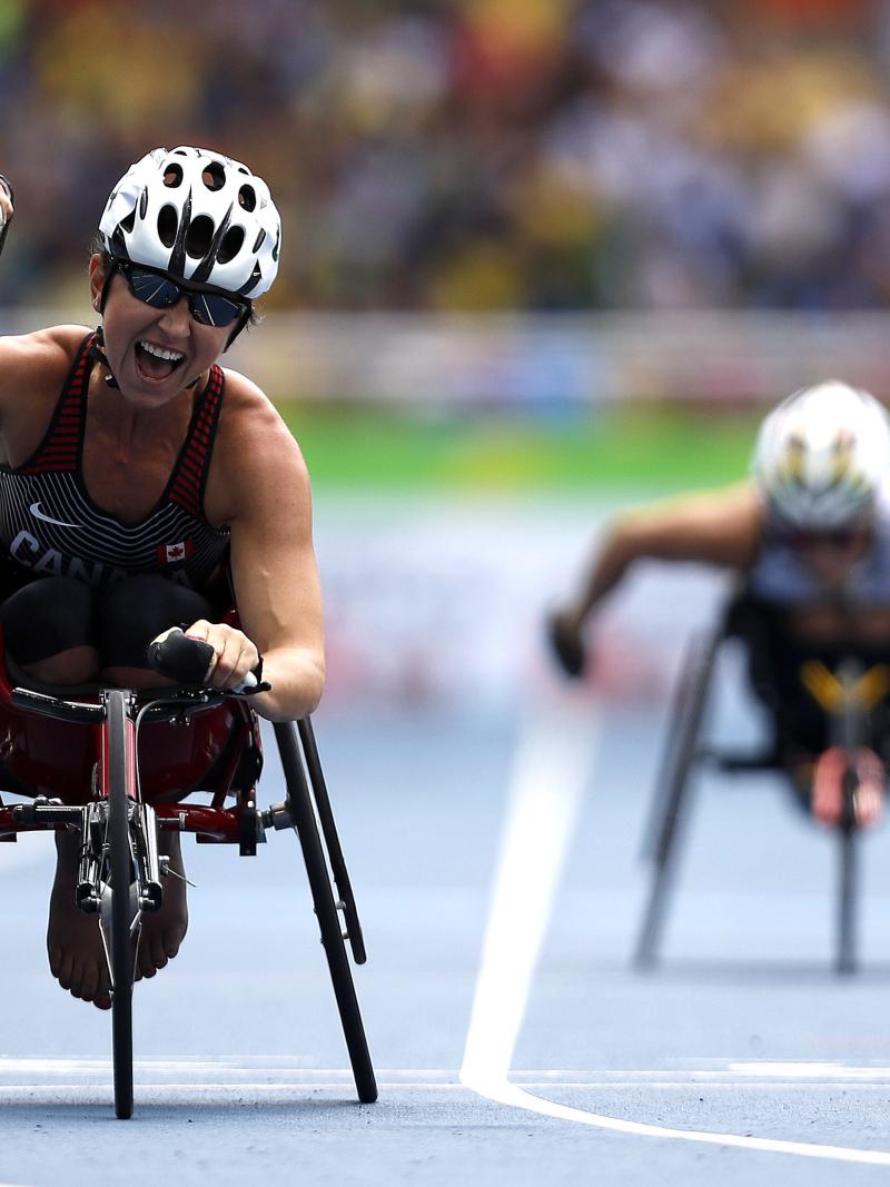 Woman in racing wheelchair crossing a finish line, celebrating