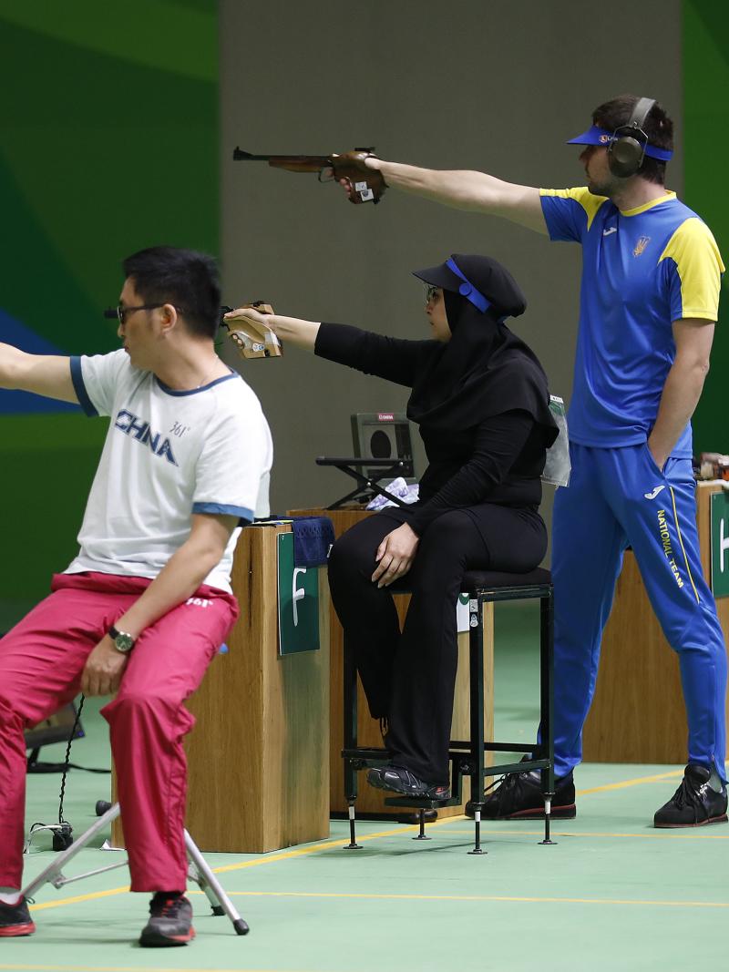 Two sitting and one standing shooting para athlete aiming at the targets