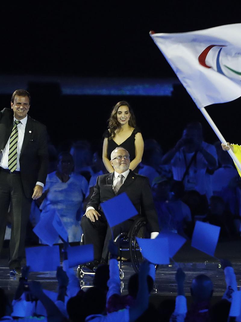Three people on a stage, one woman waving a flag