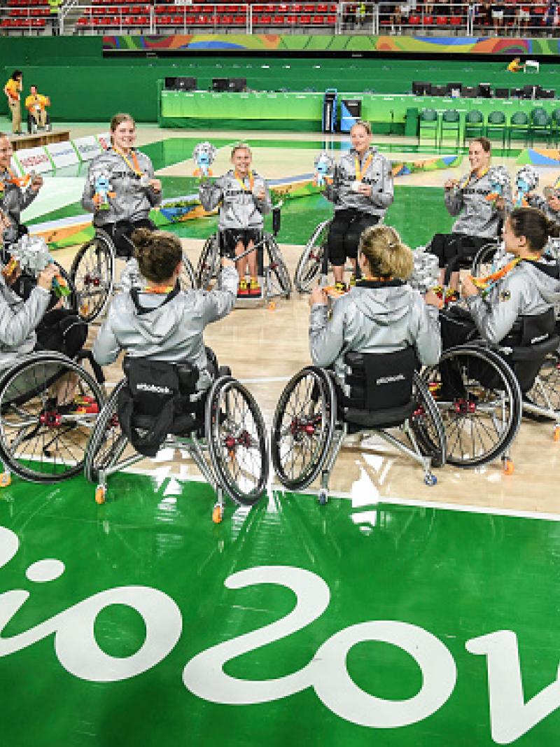 Women in wheelchairs forming a circle on a basketball field