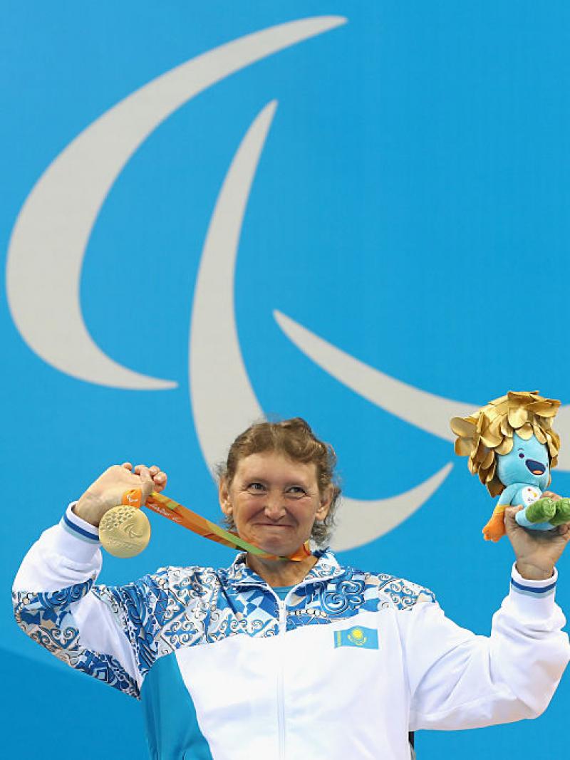 Woman on podium in a wheelchair, showing a medal