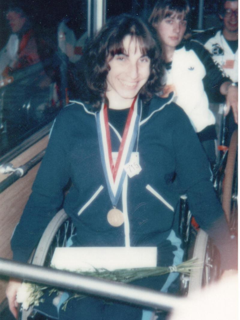 Photo of a woman in a wheelchair with a medal around her neck. The photo looks very old