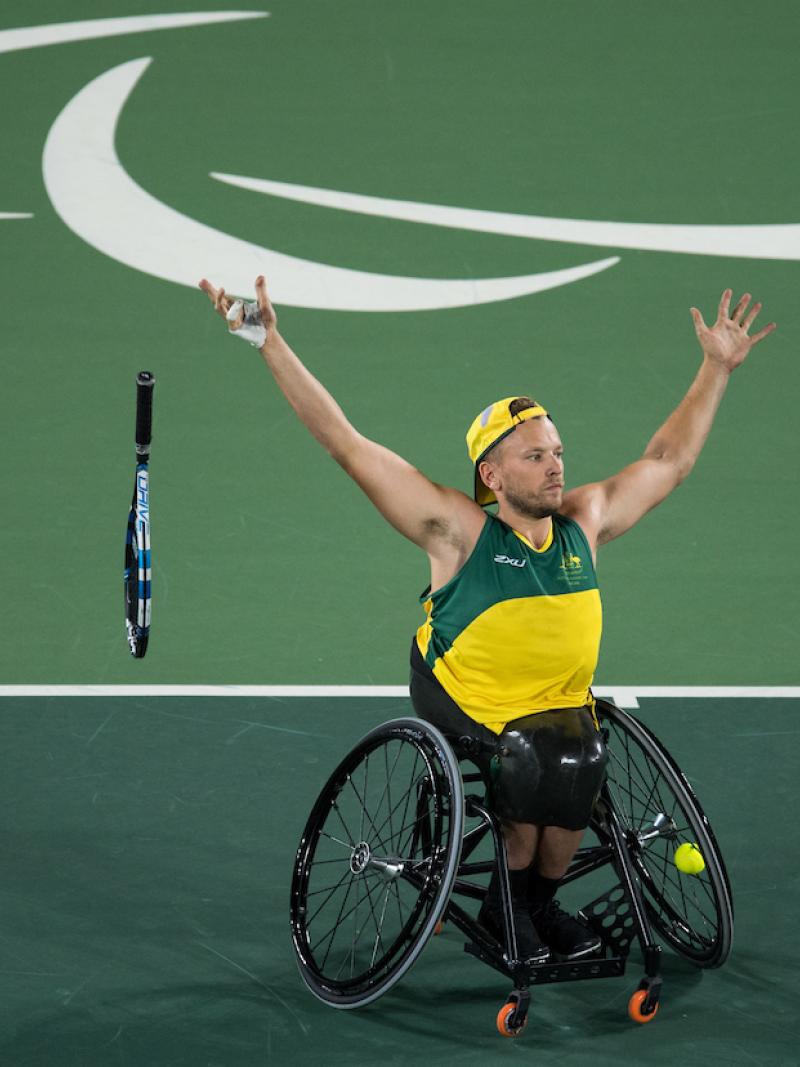 man in wheelchair throws away his tennis racket and raises his arms to celebrate
