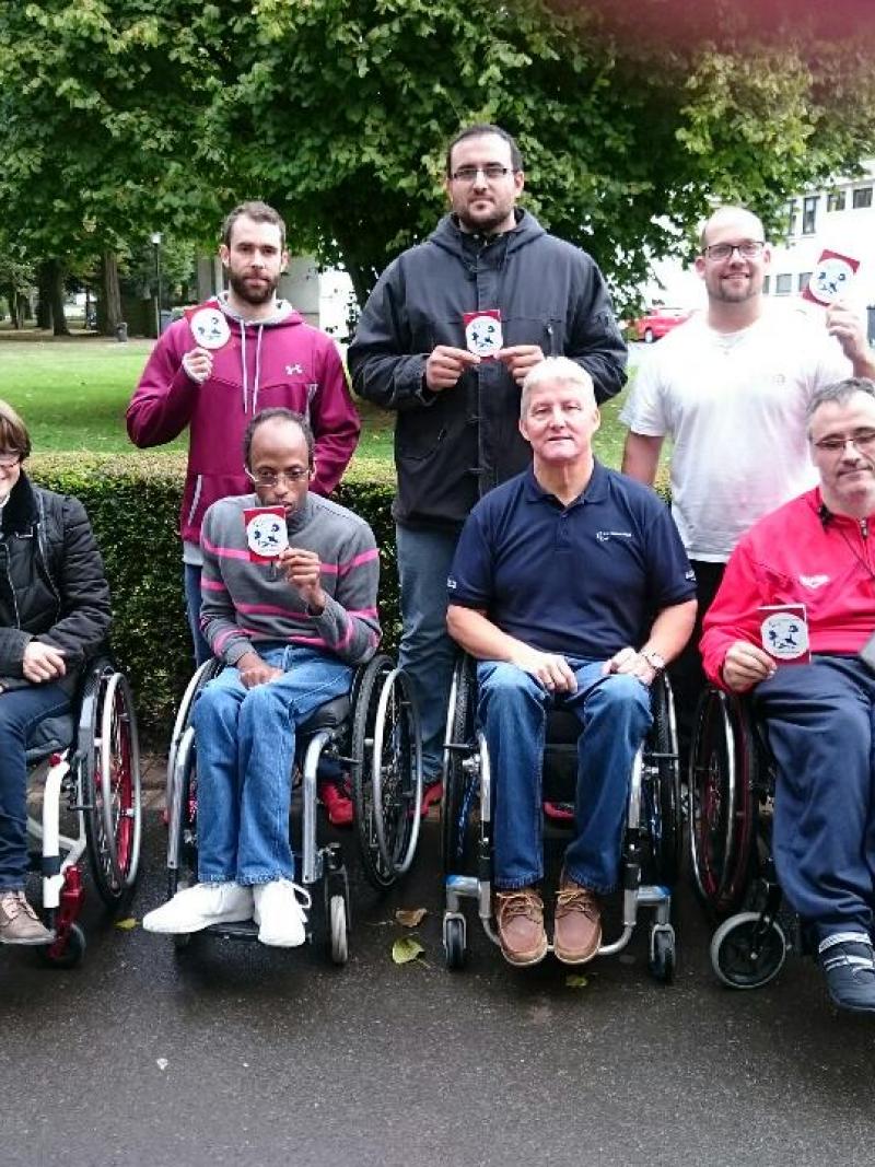 Five people in wheelchairs and standing pose with certificates