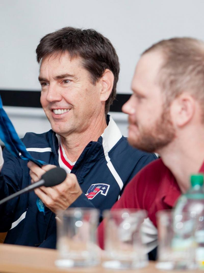 Two men on a podium, one showing a medal