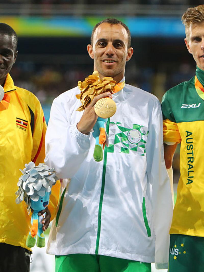 Uganda's track and field athlete David Emong celebrates on the podium with the gold and bronze medallists.