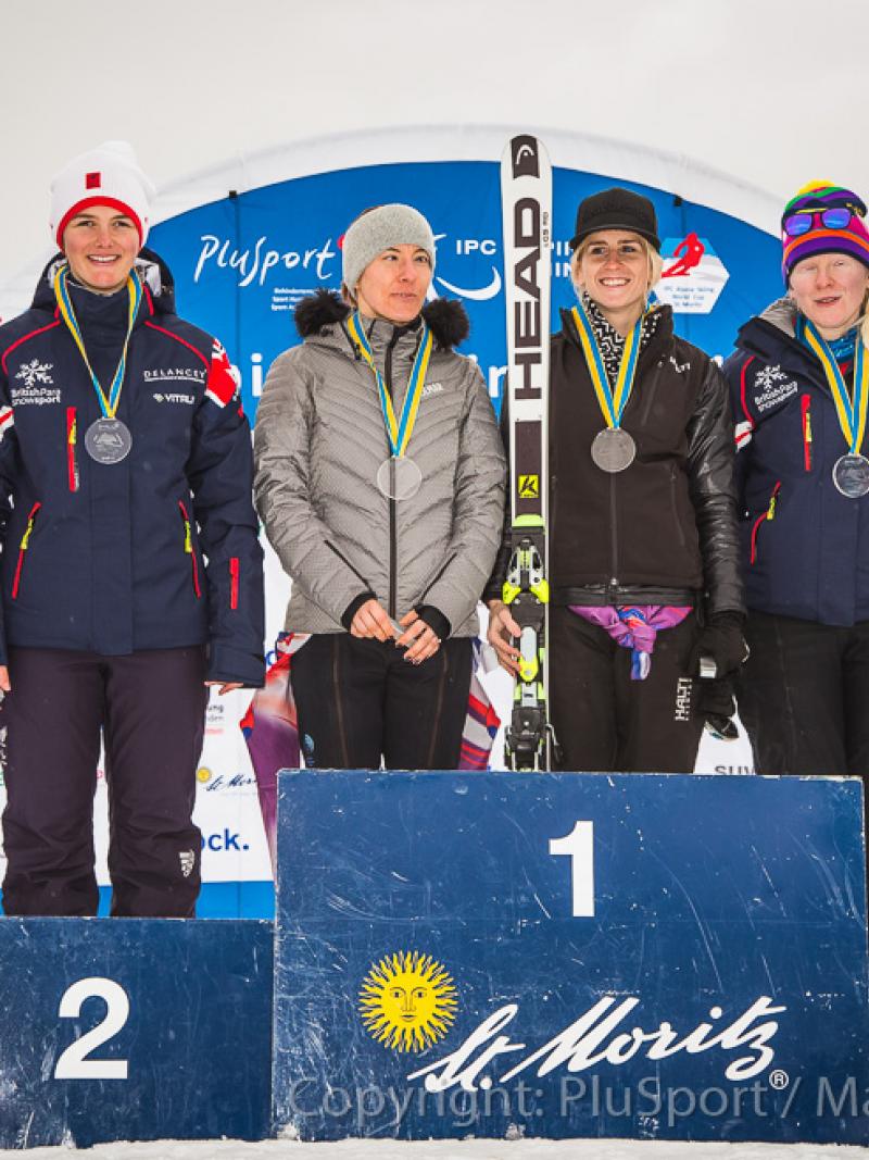 Three female alpine skiers and their guides standing on the podium