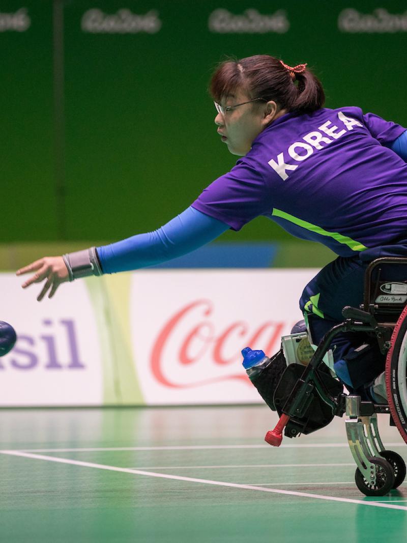 Woman in wheelchair throwing a blue boccia ball