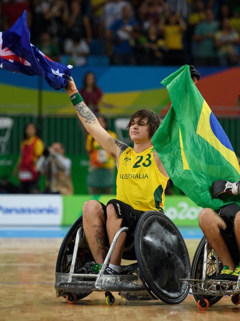 Two men in wheelchairs raise Australian and Brazilian flags. 