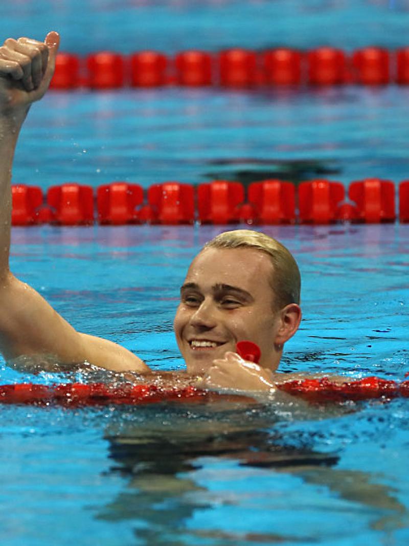 A swimmer celebrating his gold medal in the water, raising one arm.