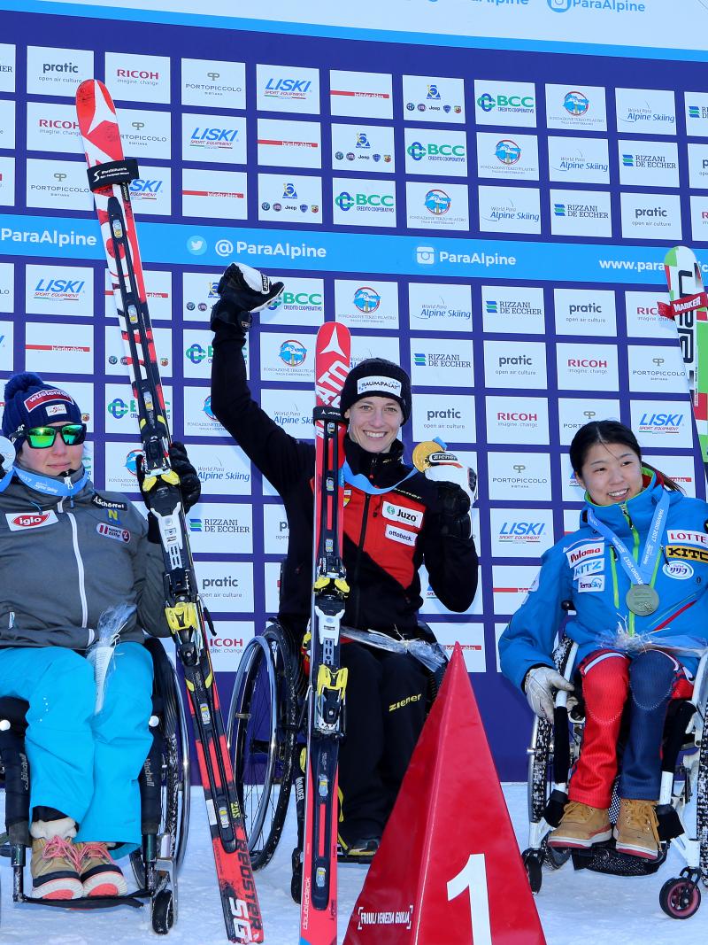 Three women in wheelchairs raising their arms with medals