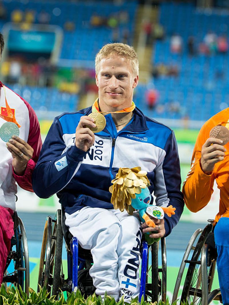 Three men in wheelchairs on a podium showing their medals