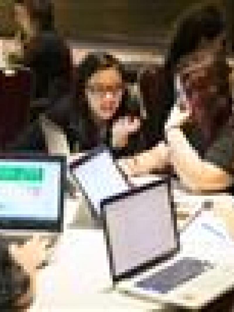 Group of young people sitting around a table with laptops, discussing