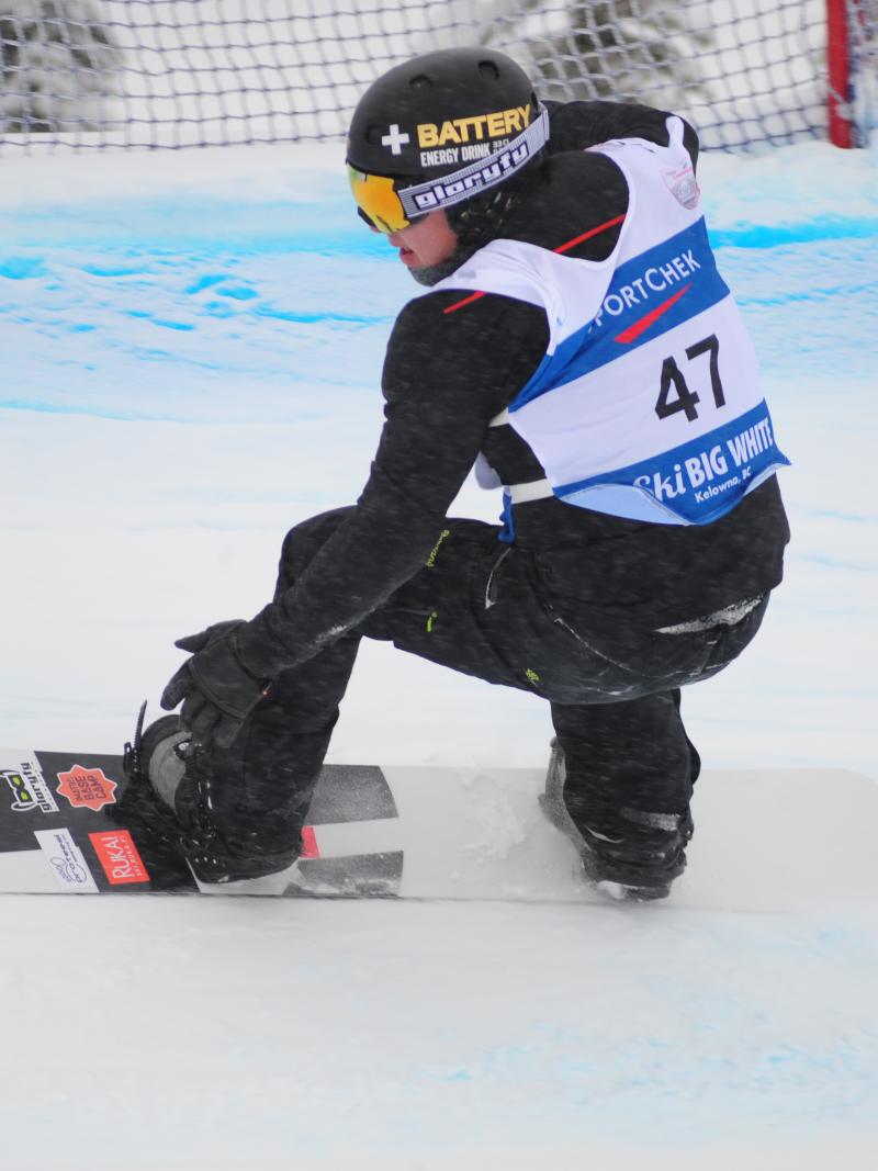 Man on snowboard rides down a snowboard-cross course.