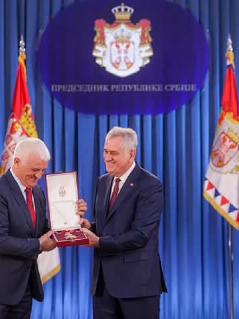 Two men on a stage, one handing a medal to the other