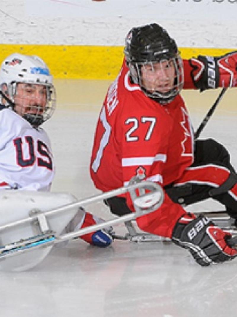 A picture of two men in sledges playing ice hockey