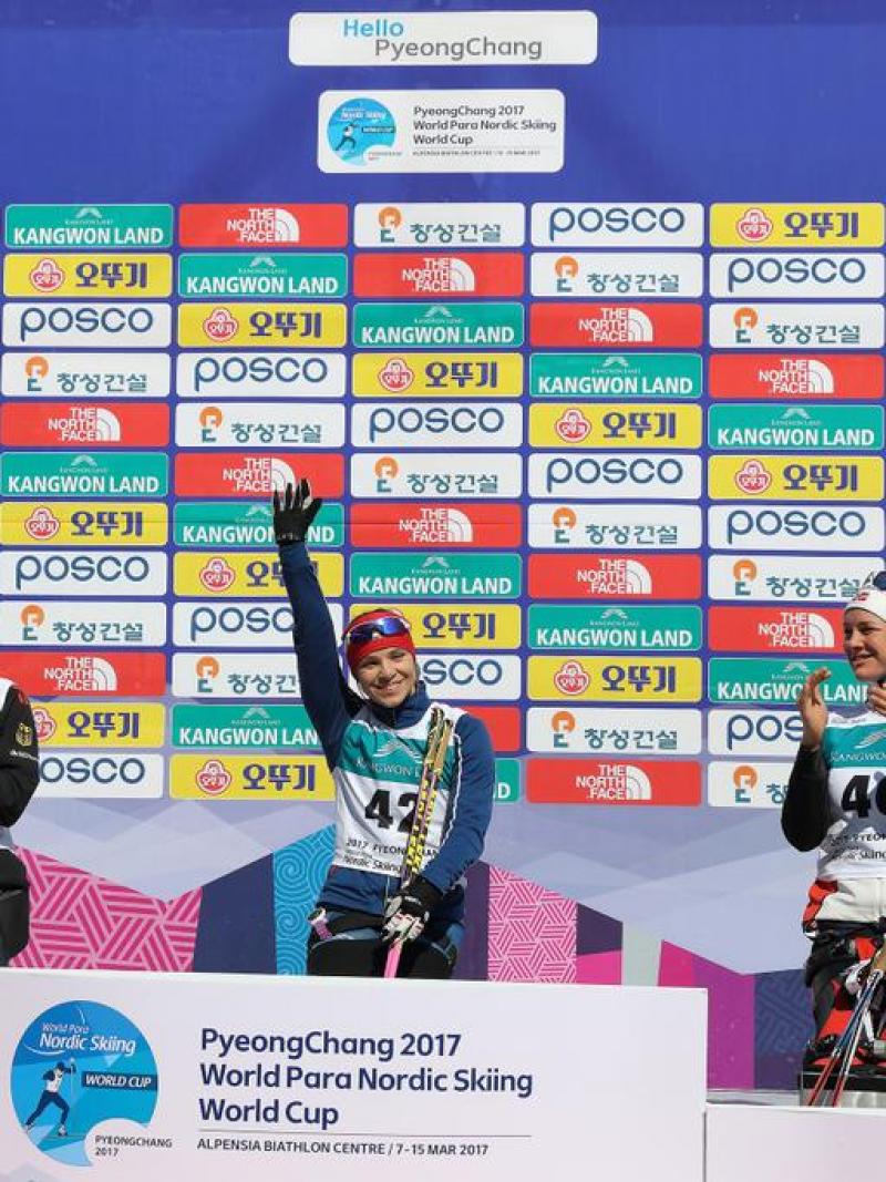 A sit skier raises her arm in the air to celebrate her victory