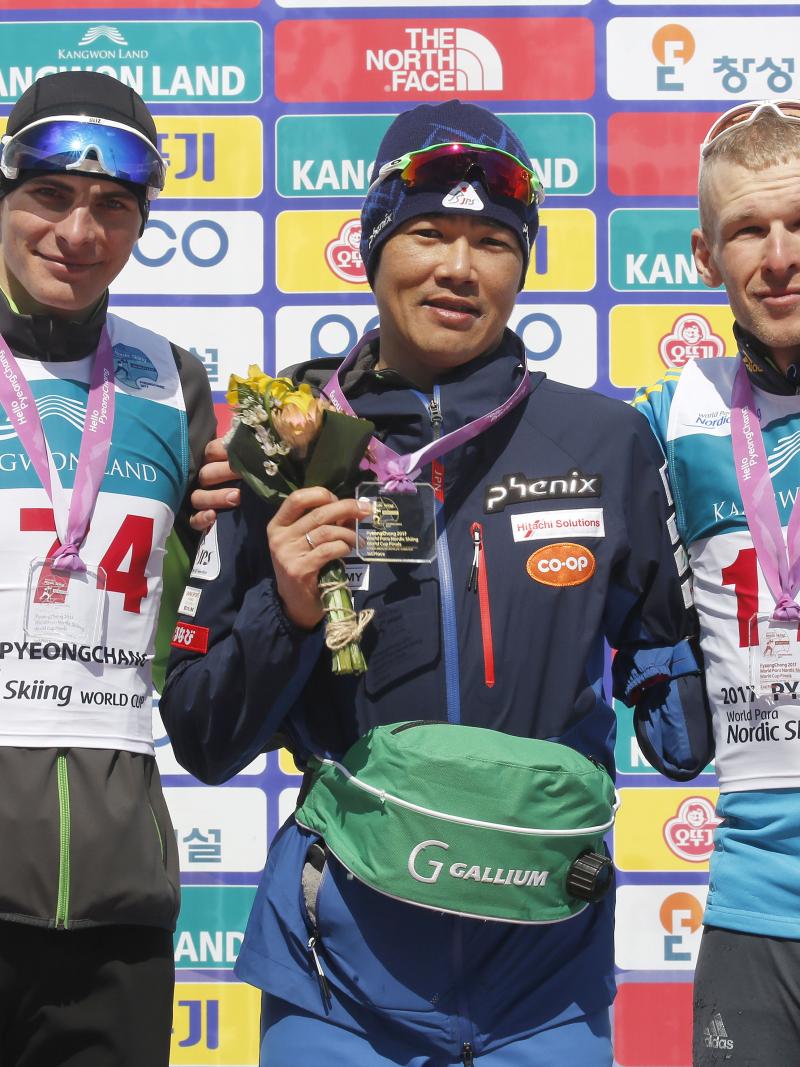 Three men on a podium, holding flower bouquets